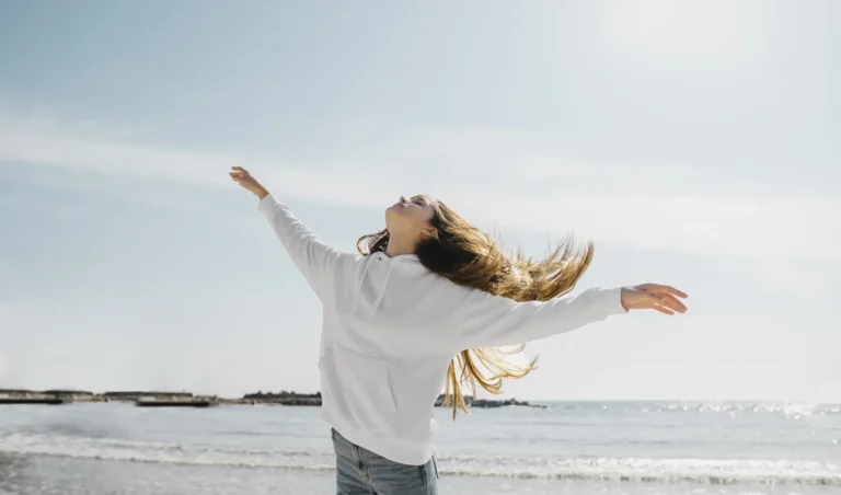 Young woman feeling freedom at the beach after a hypnotherapy session with Larissa Shaw